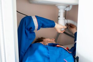 plumber in blue uniform lying in the kitchen and repair the water f